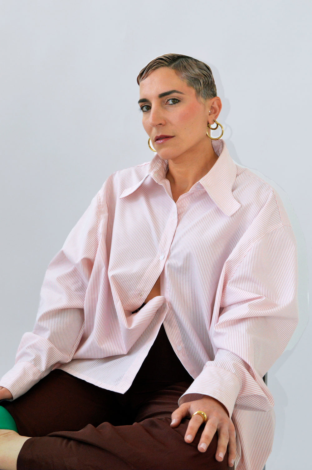 Modèle assise portant la CHEMISE TOC TOC rayée rose et blanc avec un pantalon fluide marron, évoquant un look moderne et raffiné.