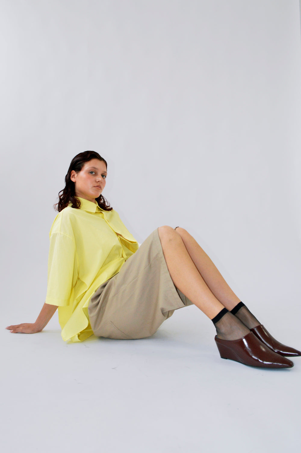 Femme assise portant la chemise PAF JAUNE à col en vague et le bermuda TRALALA SABLE, tenue décontractée et lumineuse pour l’été.