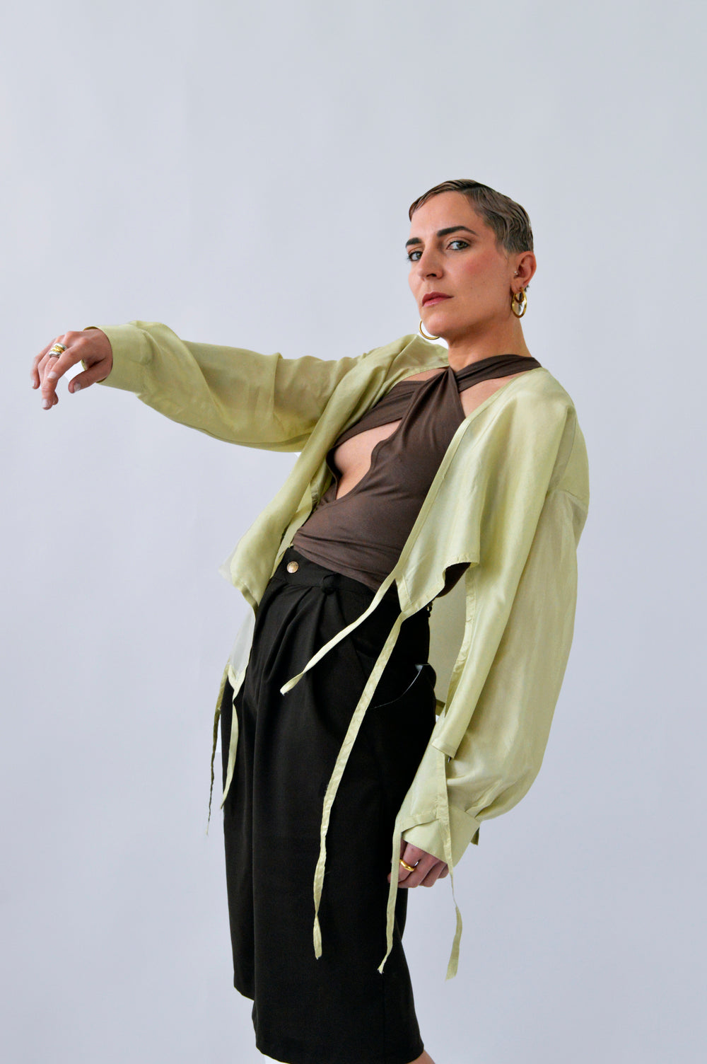 Femme portant la BLOUSE FLIP FLAP ouverte en soie verte citron, superposée à un top marron croisé et un bermuda noir, silhouette audacieuse et moderne.