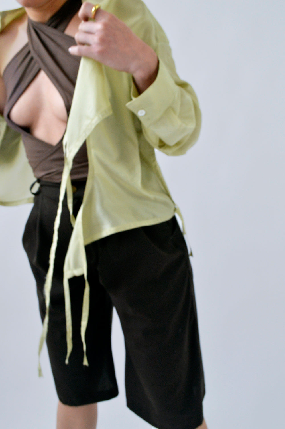 Focus détails des mouvements de la BLOUSE FLIP FLAP en soie verte citron, ouverte sur un top marron croisé et un bermuda noir.