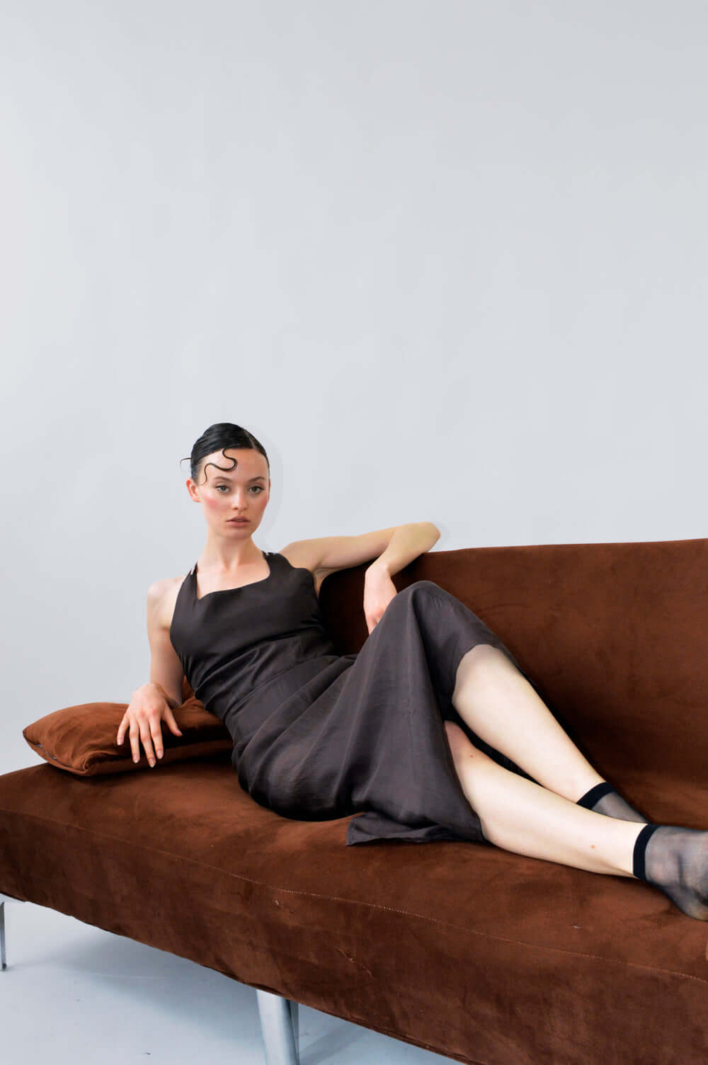 Femme portant la robe DING DONG en soie marron foncé, col droit et dos nu, allongée sur un canapé.