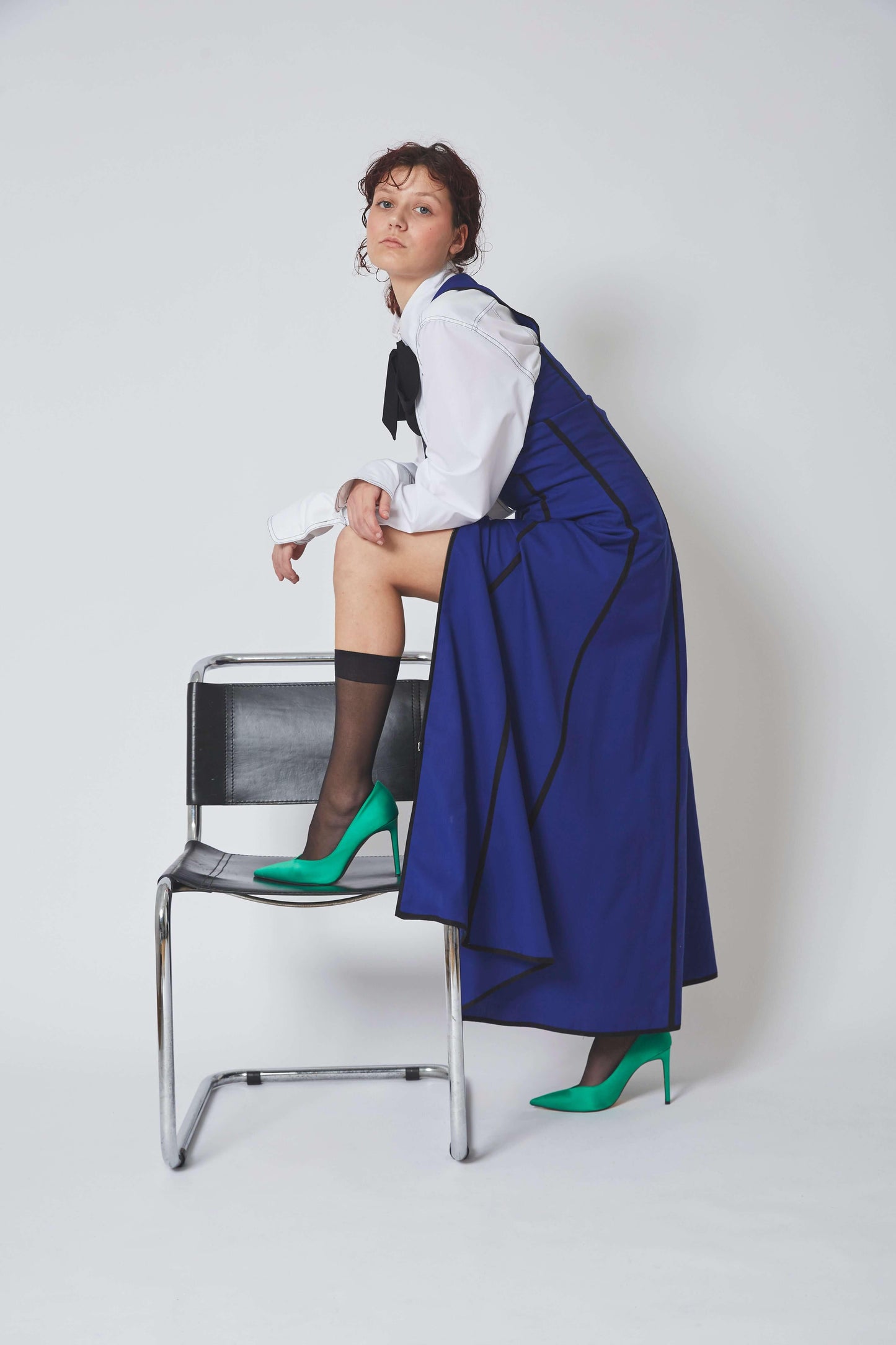 Femme portant la ROBE SERPENTINE, 100% Laine bleue, fluide et souple avec biais noir, coupe longue et cintrée.
