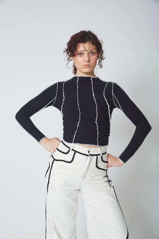 Femme portant le TOP SURJET NOIR en lycra, surpiqûres blanches, manches longues et moulant.