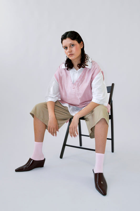 Modèle portant le TIP TOP oversize rose sans manches en viscose irisée, sur une chemise blanche et un bermuda beige, chaussettes roses et chaussures marron.