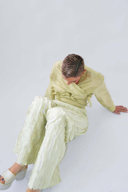 Femme assise au sol portant le PANTALON TCHAC fluide à bandes verticales et une blouse assortie en soie citron pastel, mettant en valeur la silhouette dynamique et élégante du design.