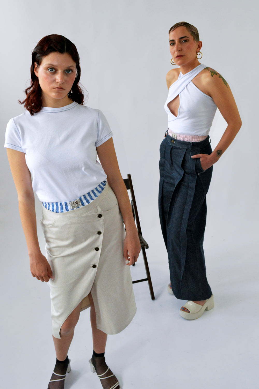 Deux femmes posant côte à côte : l’une porte le t-shirt moulant blanc à manches courtes, l’autre le débardeur blanc croisé avec surpiqûres bleues, montrant la versatilité de l’ensemble CLIC CLAC TOP.